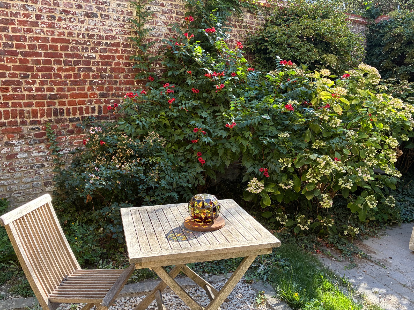 Sphère en technique Tiffany posée sur une table de jardin, devant un mur de briques