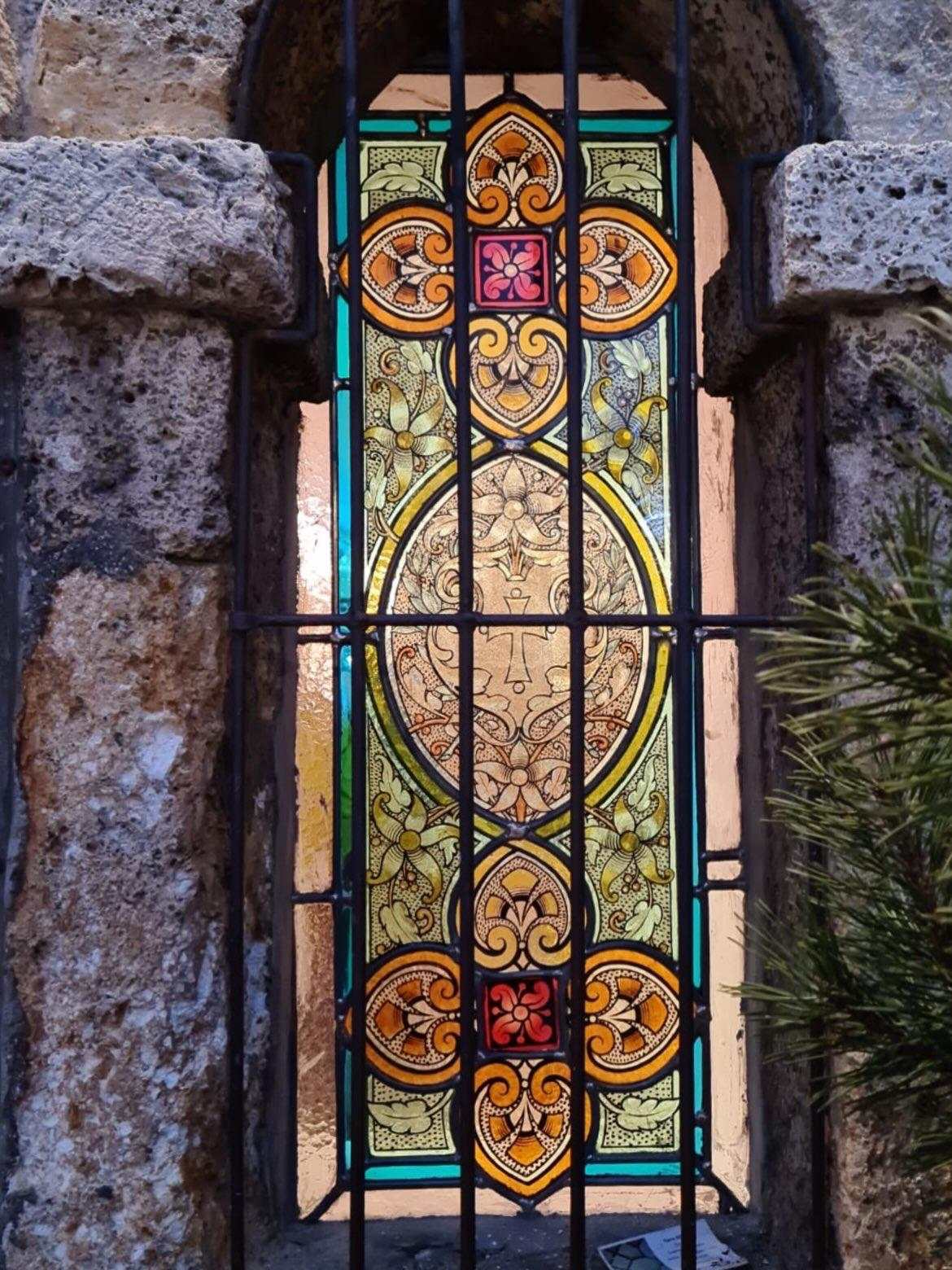 Vitrail ancien à décor floral et médaillon, posé dans une baie de pierre
